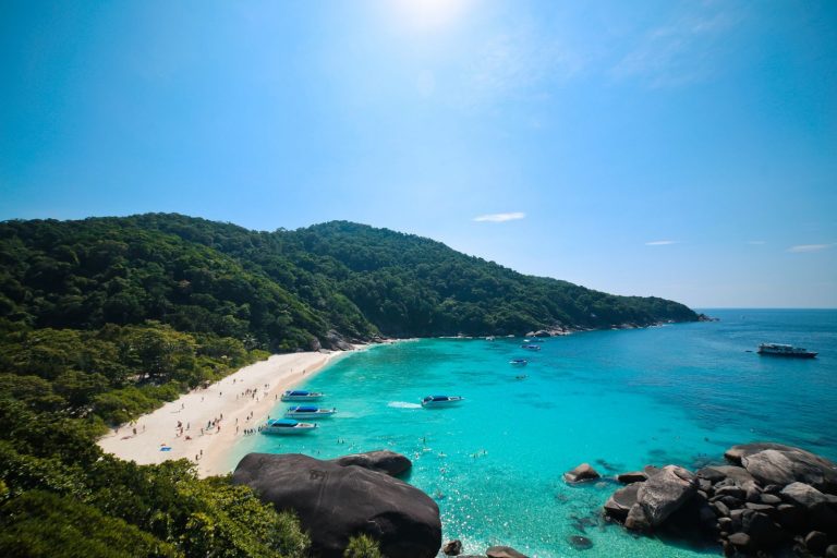 Scenic view of a tropical beach with clear blue waters and lush green hills, perfect for summer travel.